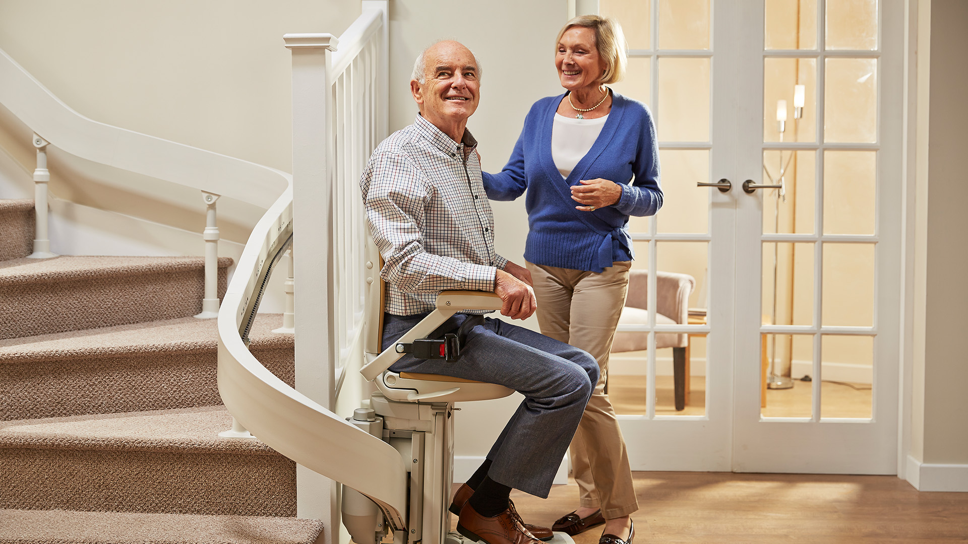 Advisor kneeling beside a smiling older woman seated in a rise & recliner chair at home